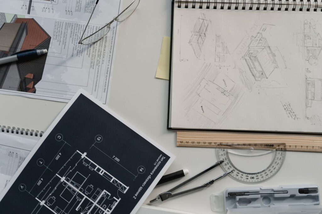 Marked-up drawings and plans spread across a desk with drafting tools