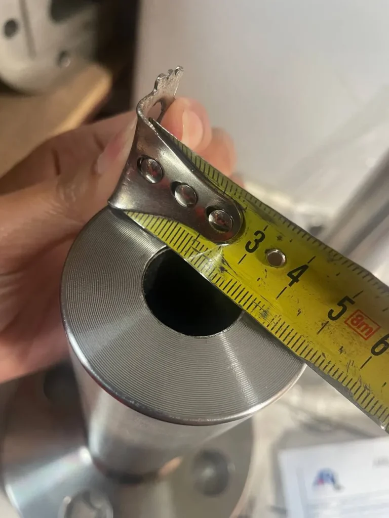 Inspector measuring a machined steel part with a tape measure during a dimensional check