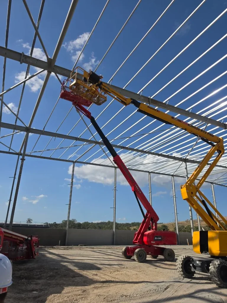 Elevated work platforms beside a steel portal frame building during erection inspection