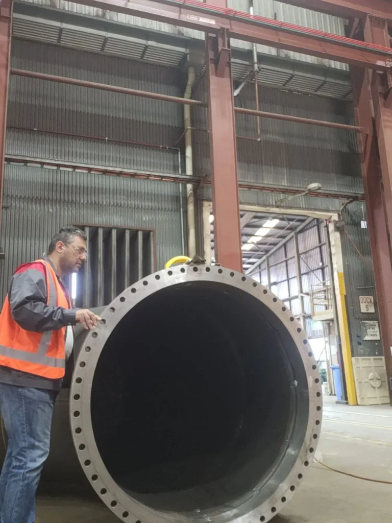 Professional Welding Clinic inspector in hi-vis carrying out a third-party inspection of a large flanged pipe in a fabrication workshop
