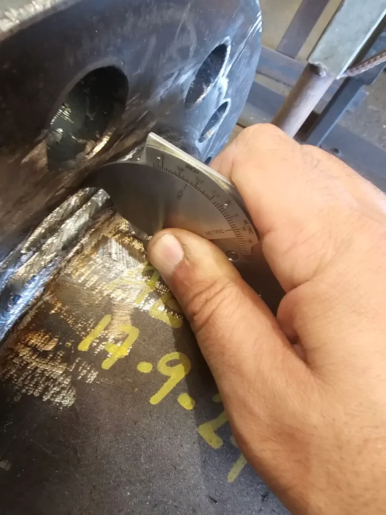 Hand holding a weld inspection gauge against a weld during visual examination training