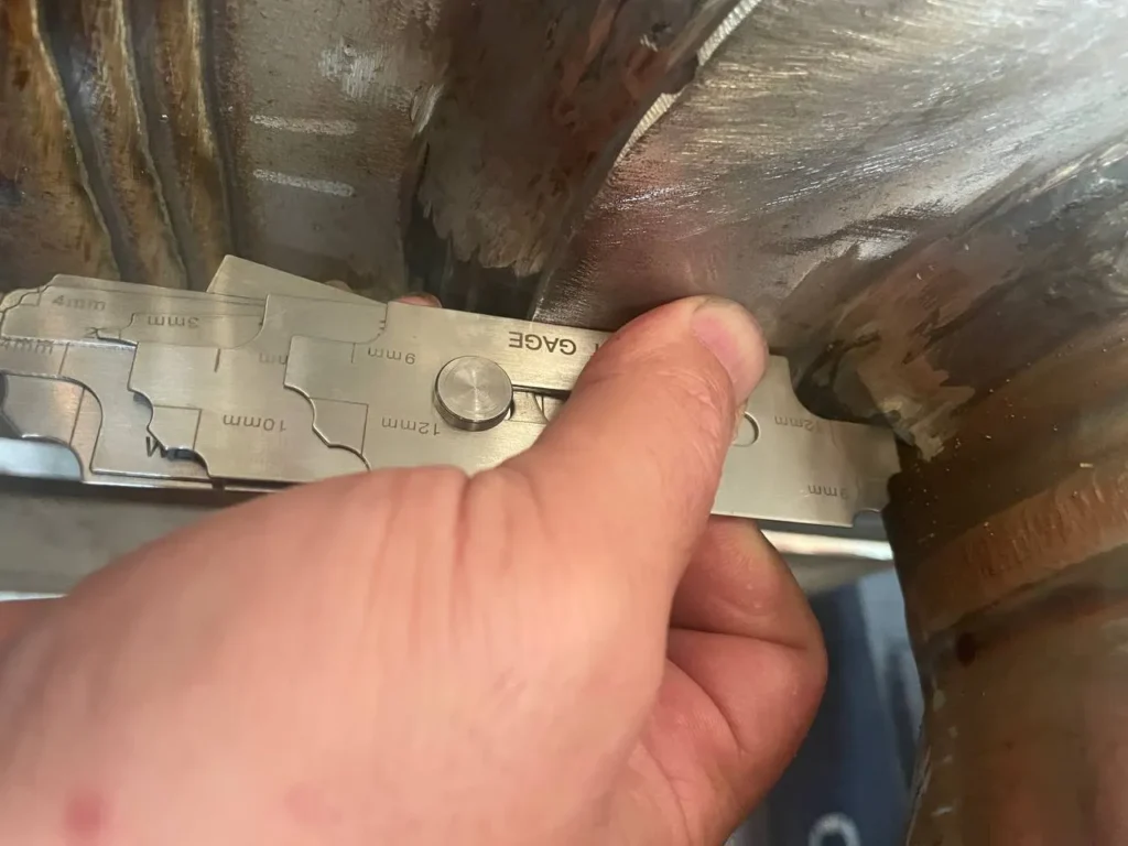 Inspector holding a fillet weld gauge against a pipe weld during visual inspection